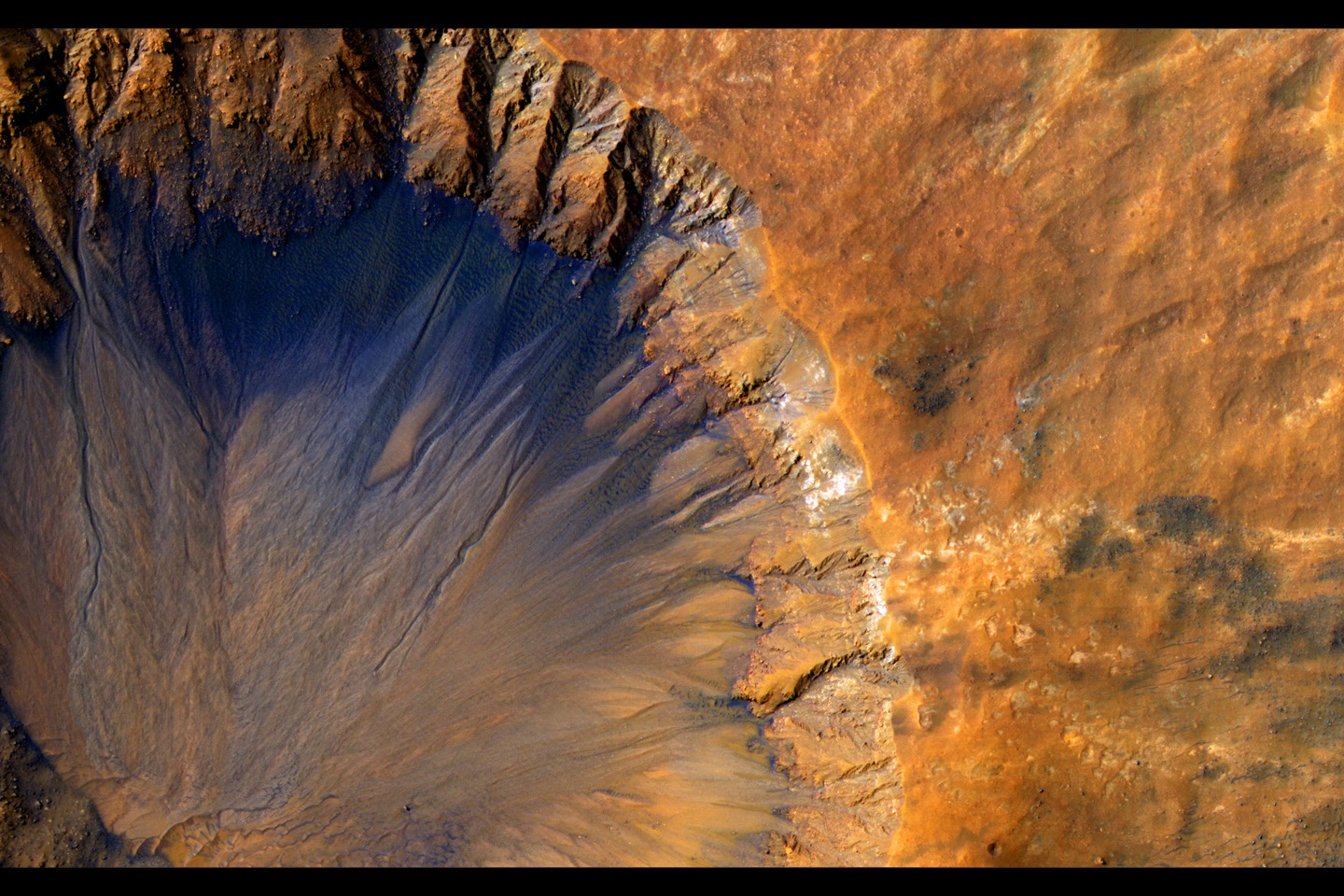 Камера HiRISE на борту Nasa Mars Reconnaissance Orbiter приобрела этот крупномасштабный образ «свежего» (в геологическом масштабе, хотя и довольно старого в человеческом масштабе) ударного кратера в регионе Сиренум Фосса на Марсе. Этот ударный кратер, шириной чуть больше 1 километра, выглядит относительно недавним, поскольку он имеет острый край и хорошо сохранившиеся выбросы.