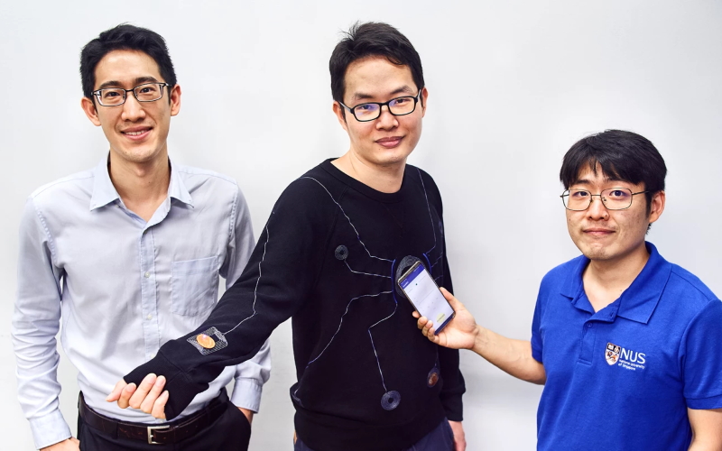Умный костюм для оценки производительности, показанный здесь ((с дизайном, напоминающим мотив костюма Человека-паука)) с доцентом John Ho (слева), доктором Lin Rongzhou (в центре) и доктором Kim Han-Joon (справа).